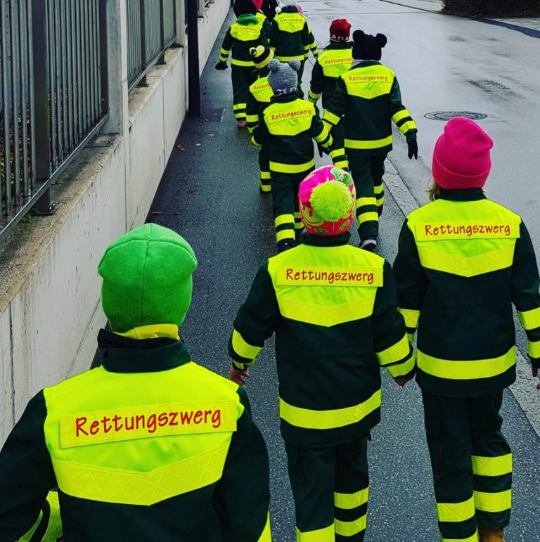Grupa djece u sigurnosnim prslucima s natpisom „Rettungszwerg“ na putu.