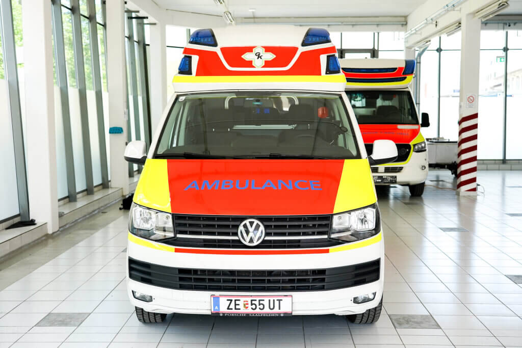 Rote und gelbe Ambulanz mit der Aufschrift "AMBULANCE" in einer modernen Halle.